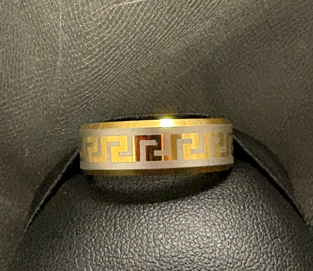 Gold and silver ring with Greek key design on a textured gray surface