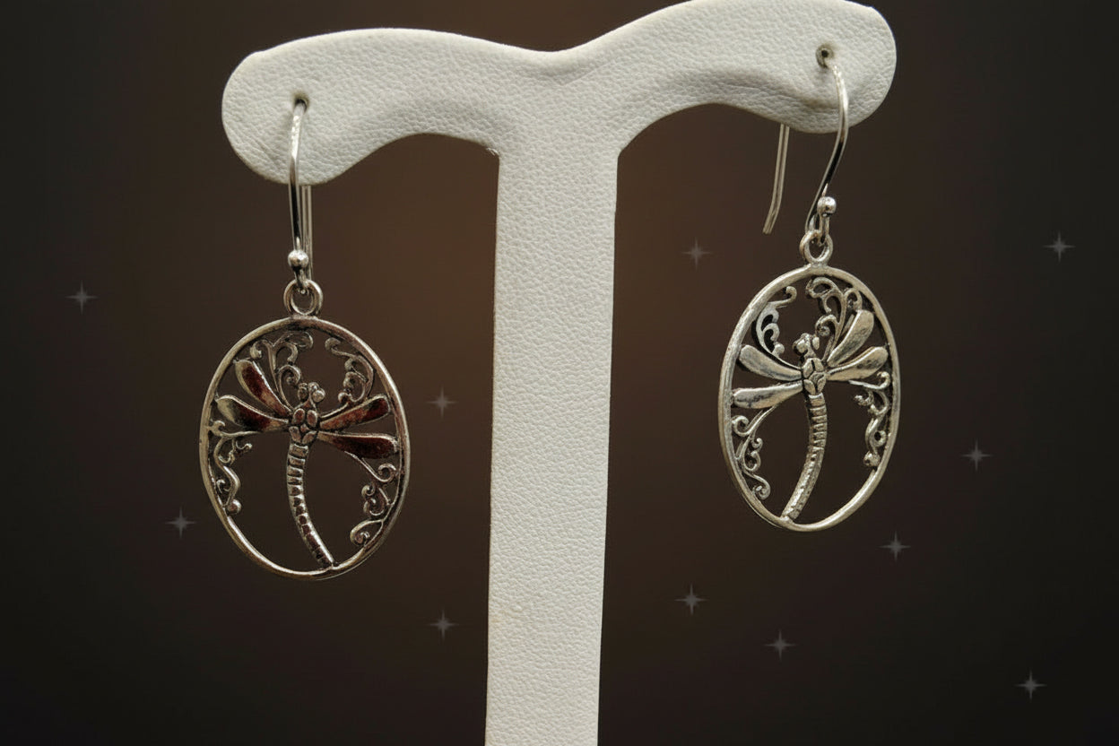 Silver dragonfly earrings on a white earring stand against a gray background