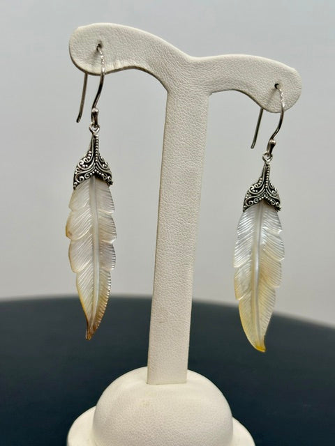 Feather-shaped earrings on a white earring stand against a gray background