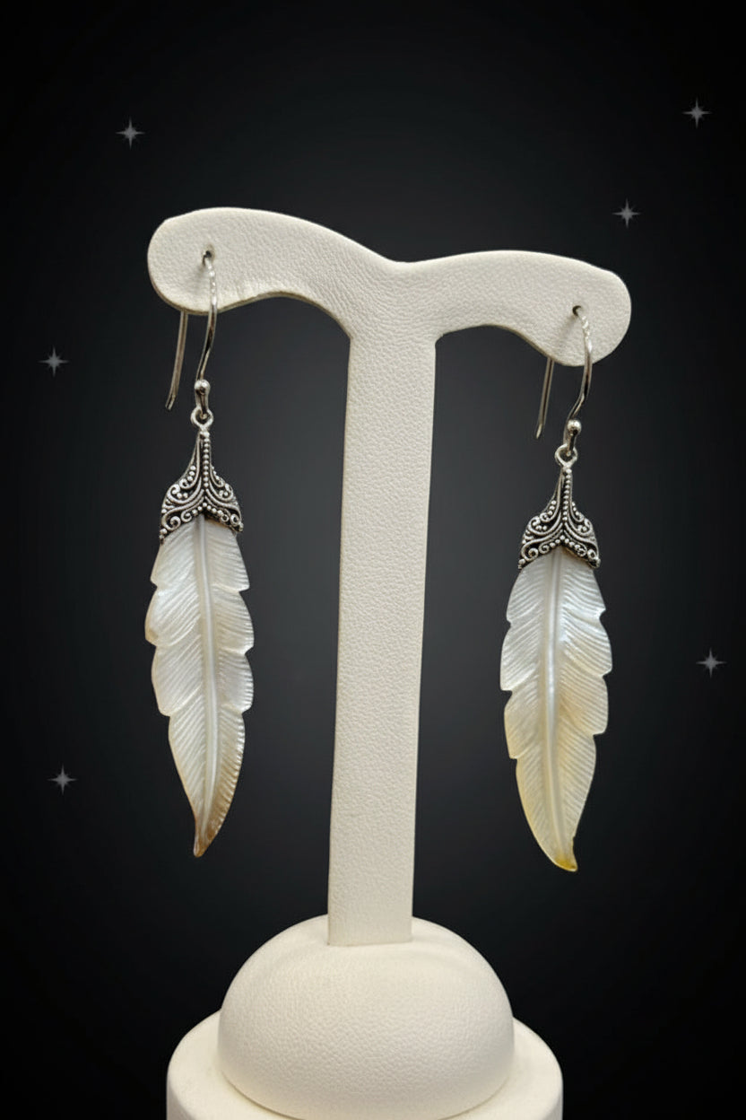 Feather-shaped earrings on a white earring stand against a gray background