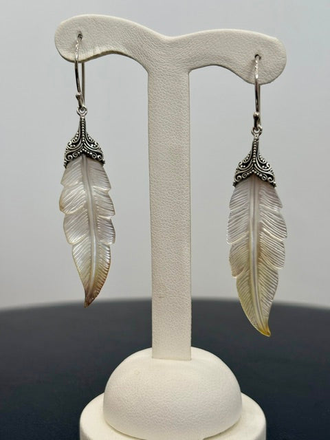 Feather-shaped earrings on a white stand against a gray background