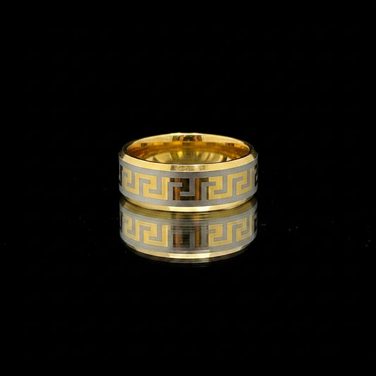 Gold and silver ring with Greek key design on a textured gray surface