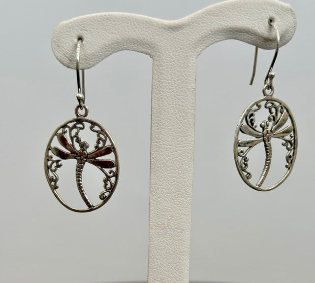 Silver dragonfly earrings on a white earring stand against a gray background