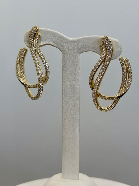 Gold colored hoop earrings with clear stones on a white stand against a gray background