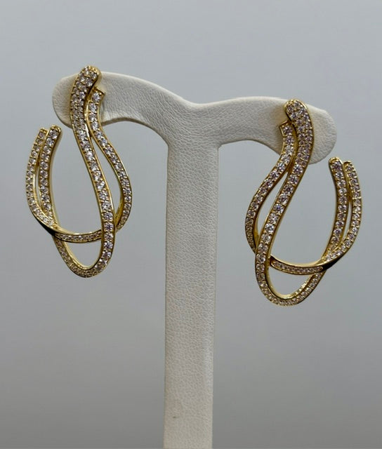 Gold colored dangle earrings with clear stones on a white stand against a gray background
