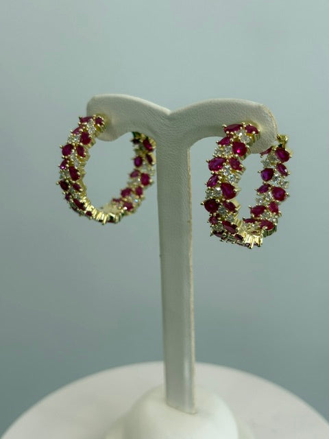 Gold earrings with red gemstones on a white stand against a gray background