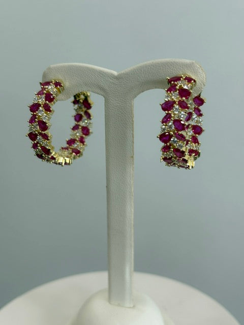 Gold and red gemstone earrings on a white stand against a gray background