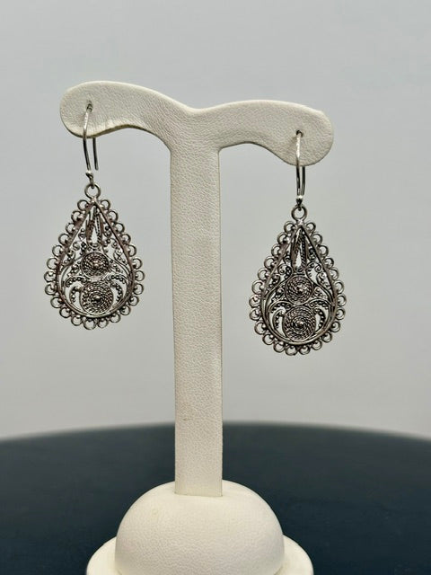Pair of silver filigree earrings on a white stand against a gray background