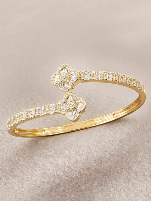 Gold clover design bangle with diamond accents on a beige background